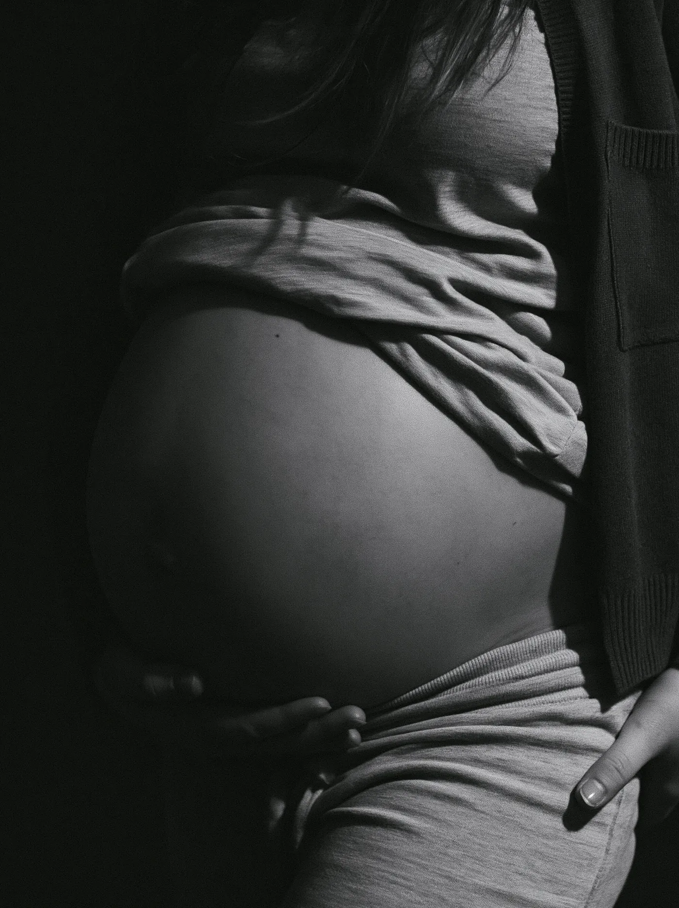 Black and white close study of a pregnant belly in low directional light
