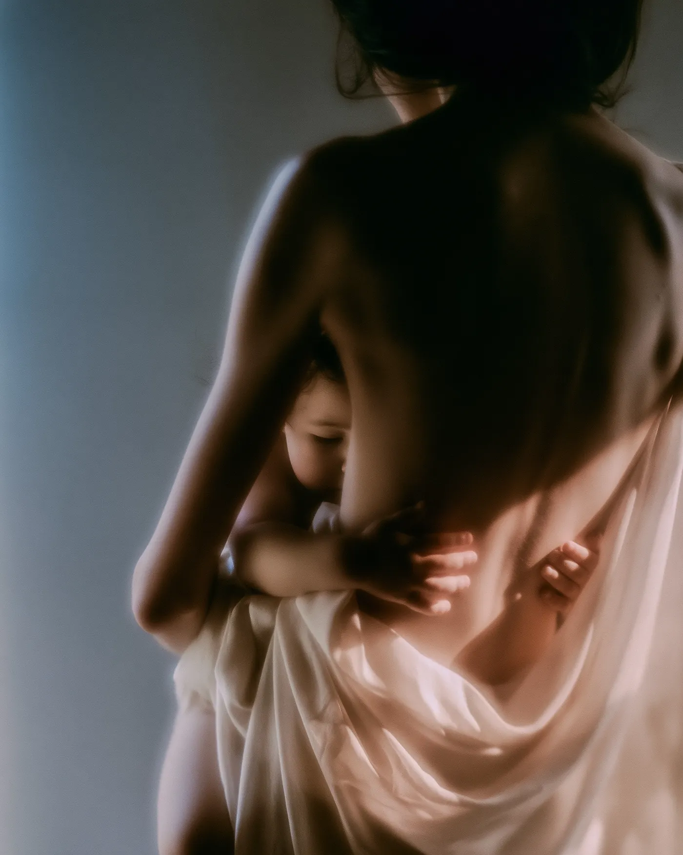 Mother holding her twelve week old baby against her shoulder in soft window light